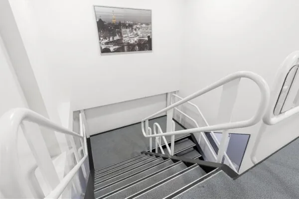 Witgeschilderd trappenhuis met grijze vloerbedekking en een ingelijste zwart-witfoto van Parijs aan de muur.